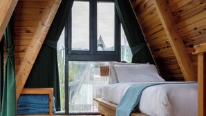 A cozy attic bedroom with a wooden sloped ceiling, a large window, and a bed with white bedding. - Yeşil Düş Bungalov (Findikli)