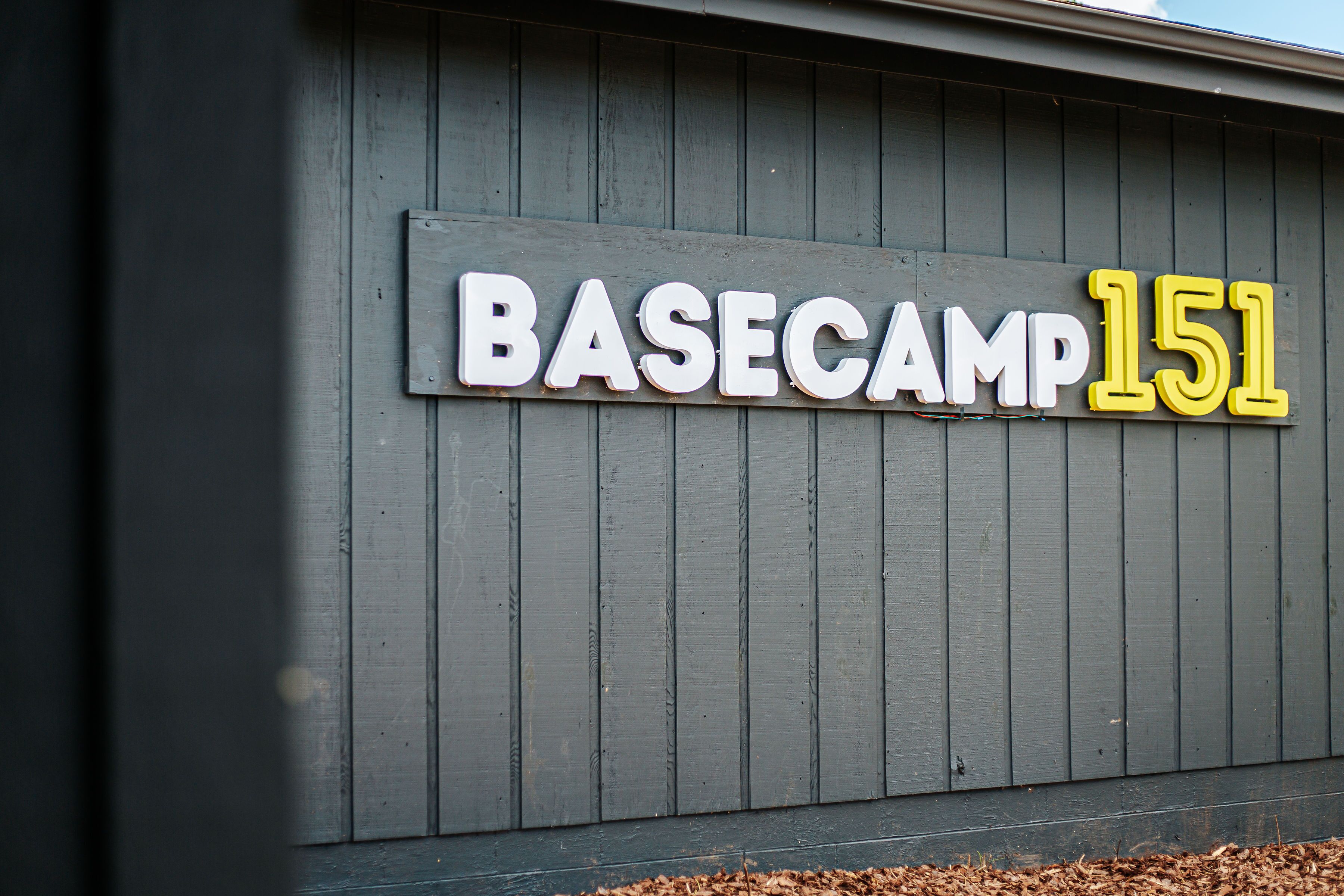 A building with a sign that reads "BASECAMP 151" on a gray wooden wall.