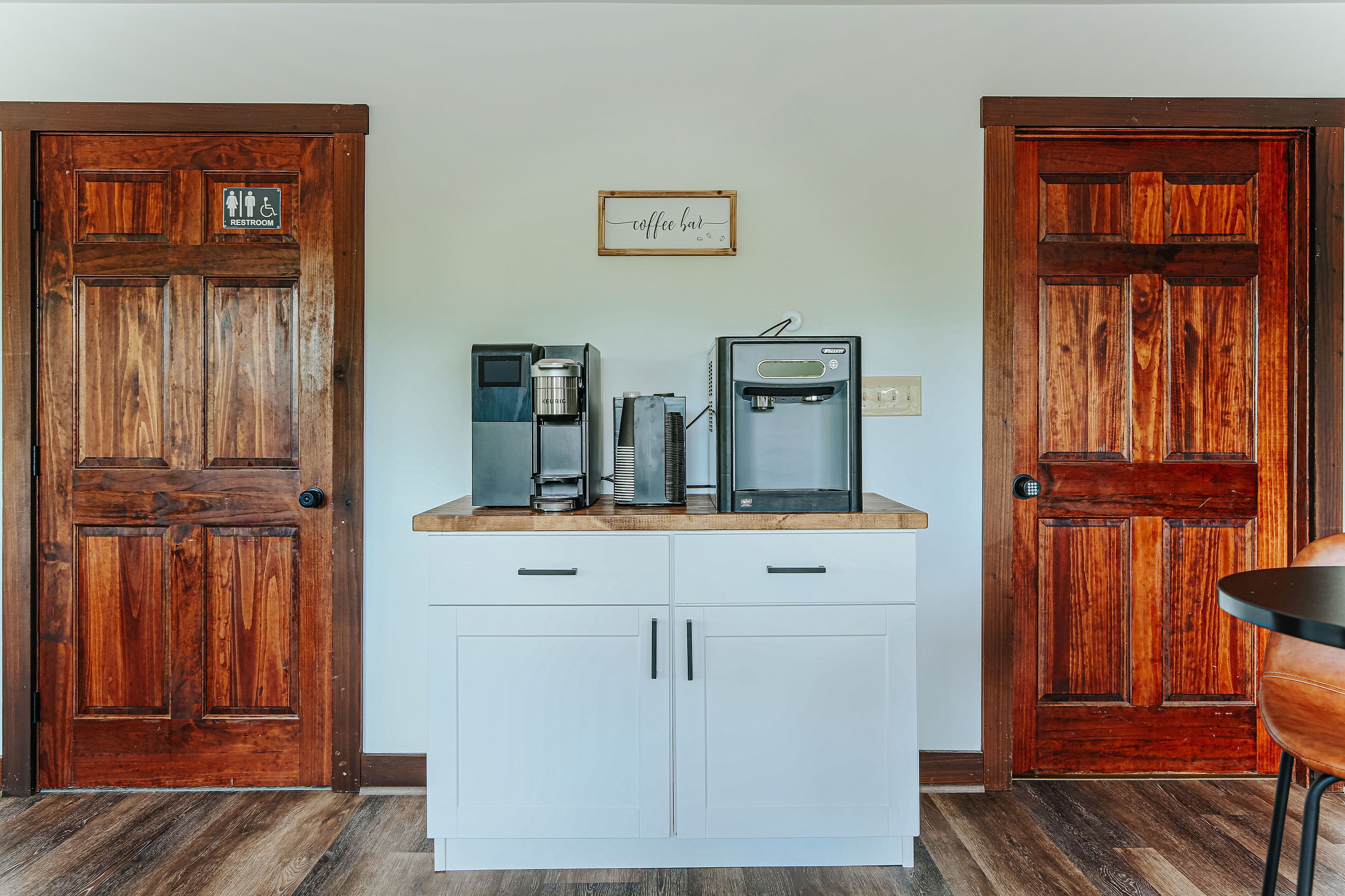 A kitchenette with a coffee machine and water dispenser, two wooden doors, and a sign above the coffee machine.