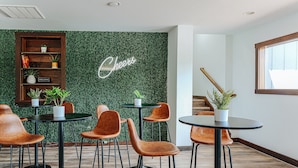 A modern indoor space with a green wall, a 'Cheers' sign, and several tables and chairs. - Basecamp151 (Afton)