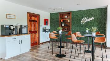A modern kitchen with a coffee station, a wooden door, and a green wall with a 'Cheers' sign.