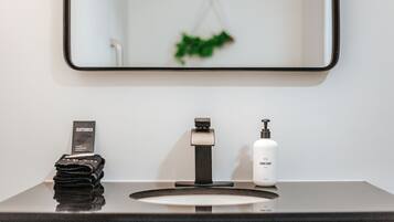 A bathroom with a black countertop, a sink with a modern faucet, a soap dispenser, and a mirror with a green plant reflection.