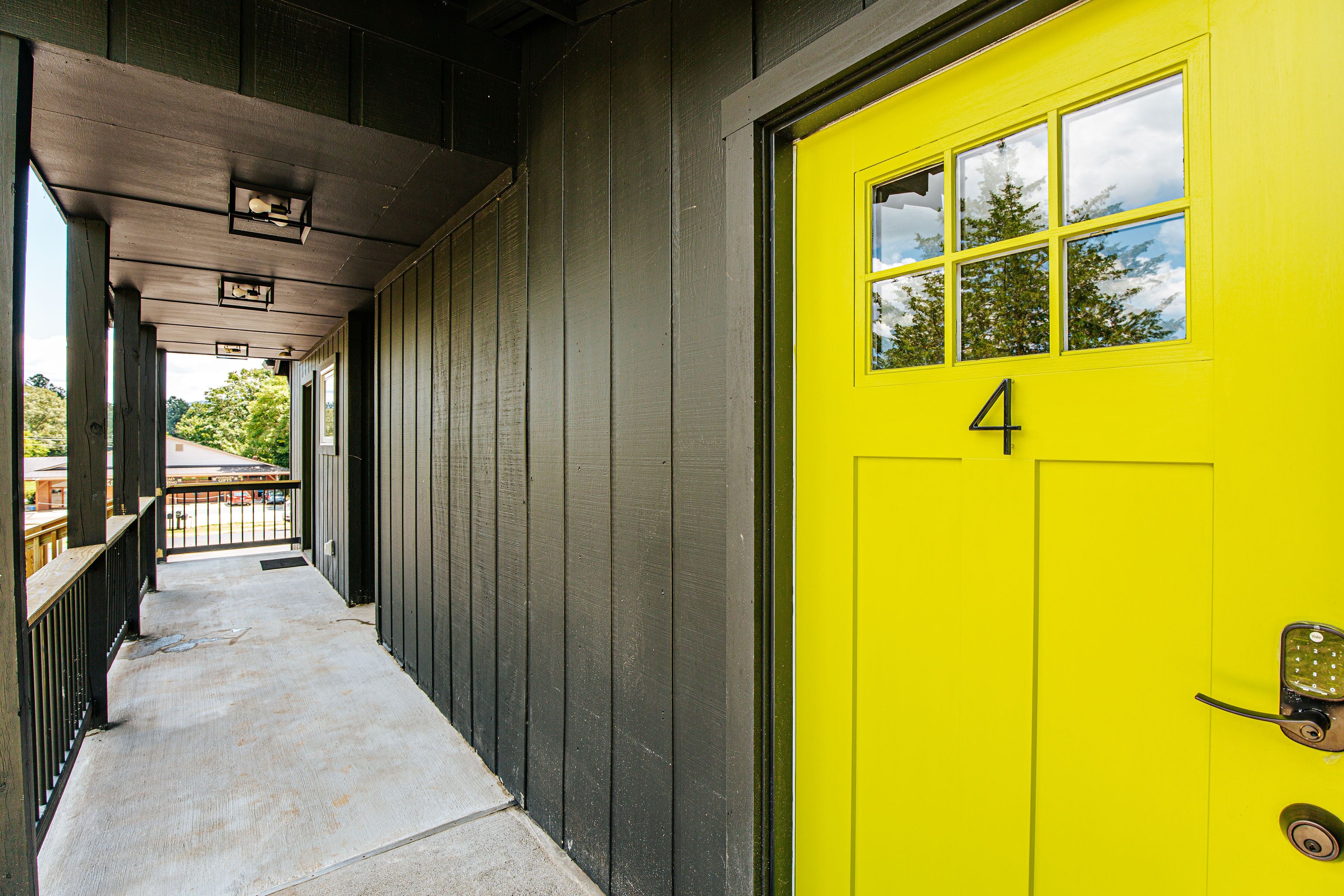 Un bâtiment avec une porte jaune vif portant le numéro 4, une allée couverte et une vue sur des arbres et un autre bâtiment en arrière-plan.