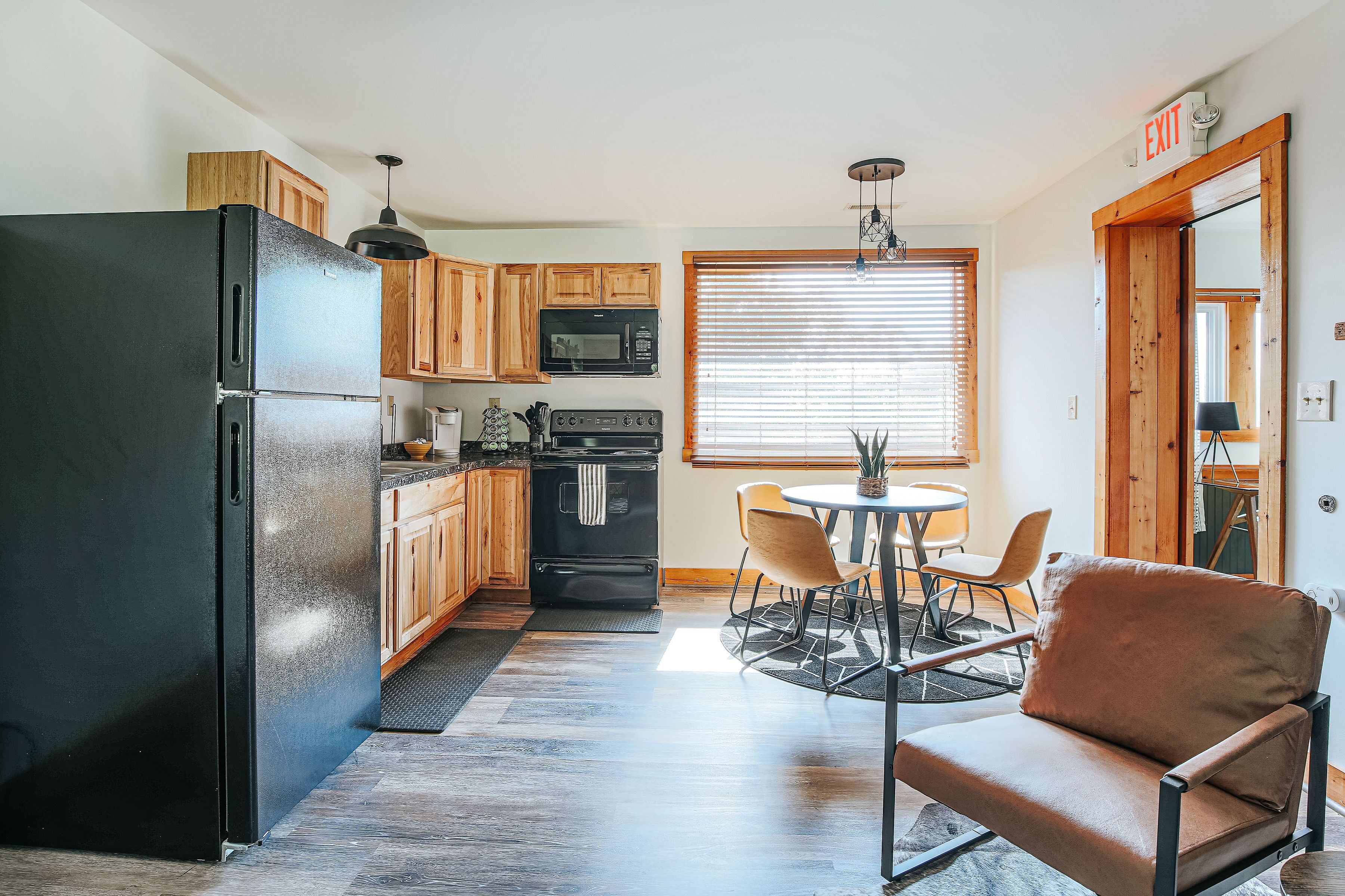 A kitchen with wooden cabinets, a black refrigerator, a microwave, and a stove. There is a dining area with a round table and chairs.