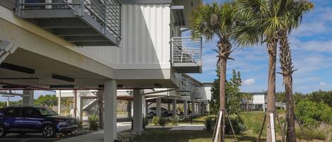 A modern building with a covered parking area, a staircase, and palm trees.