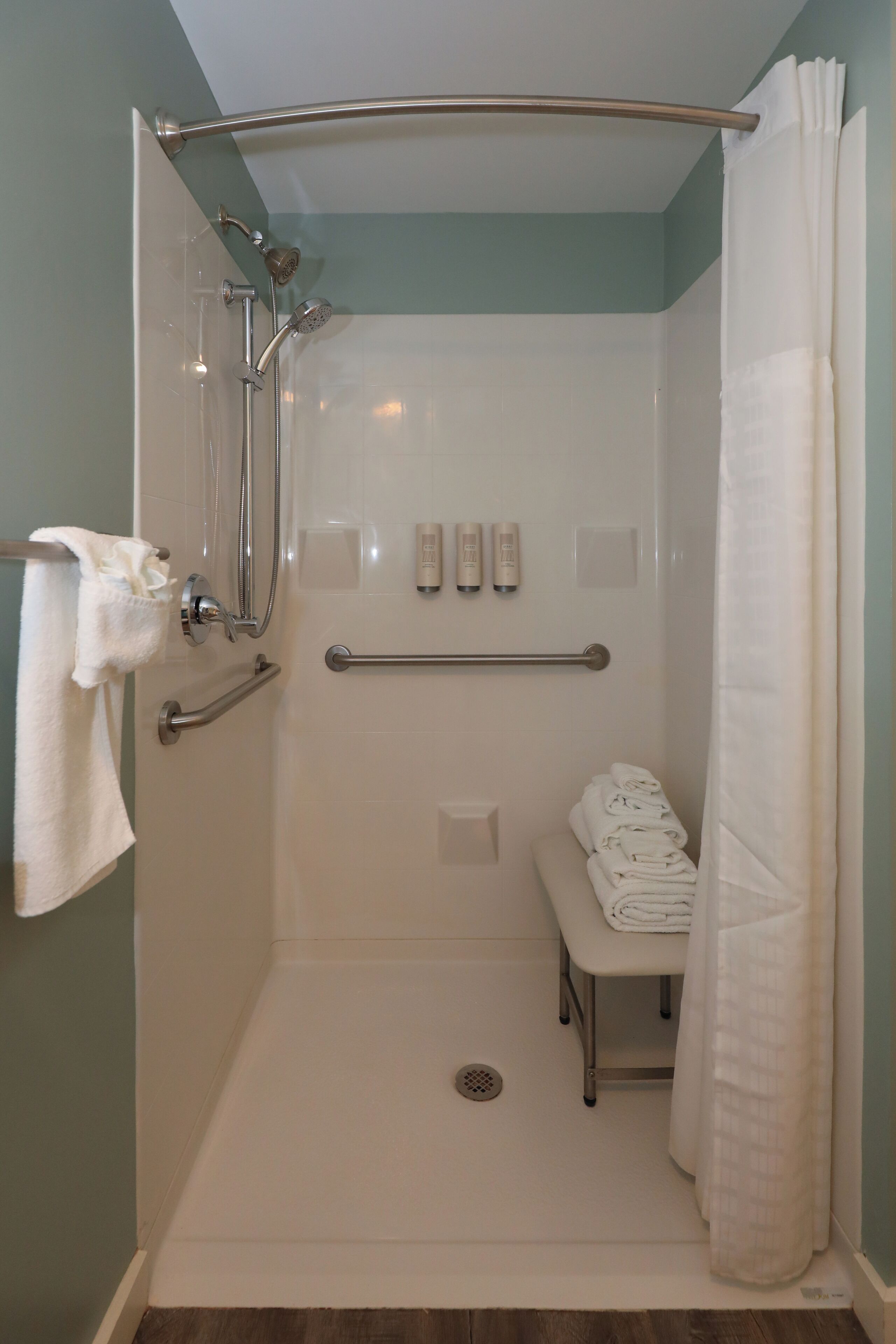 Une douche à l’italienne avec une porte en verre, une barre d’appui, un banc et un porte-serviettes.