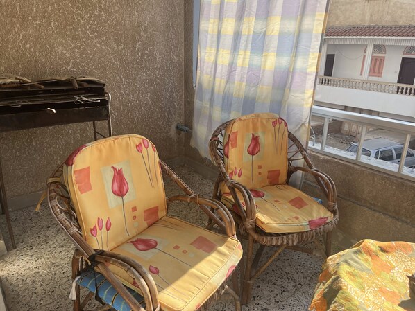 Ein Balkon mit zwei Korbstühlen, einem Tisch und Blick auf ein Gebäude mit Balkonen.