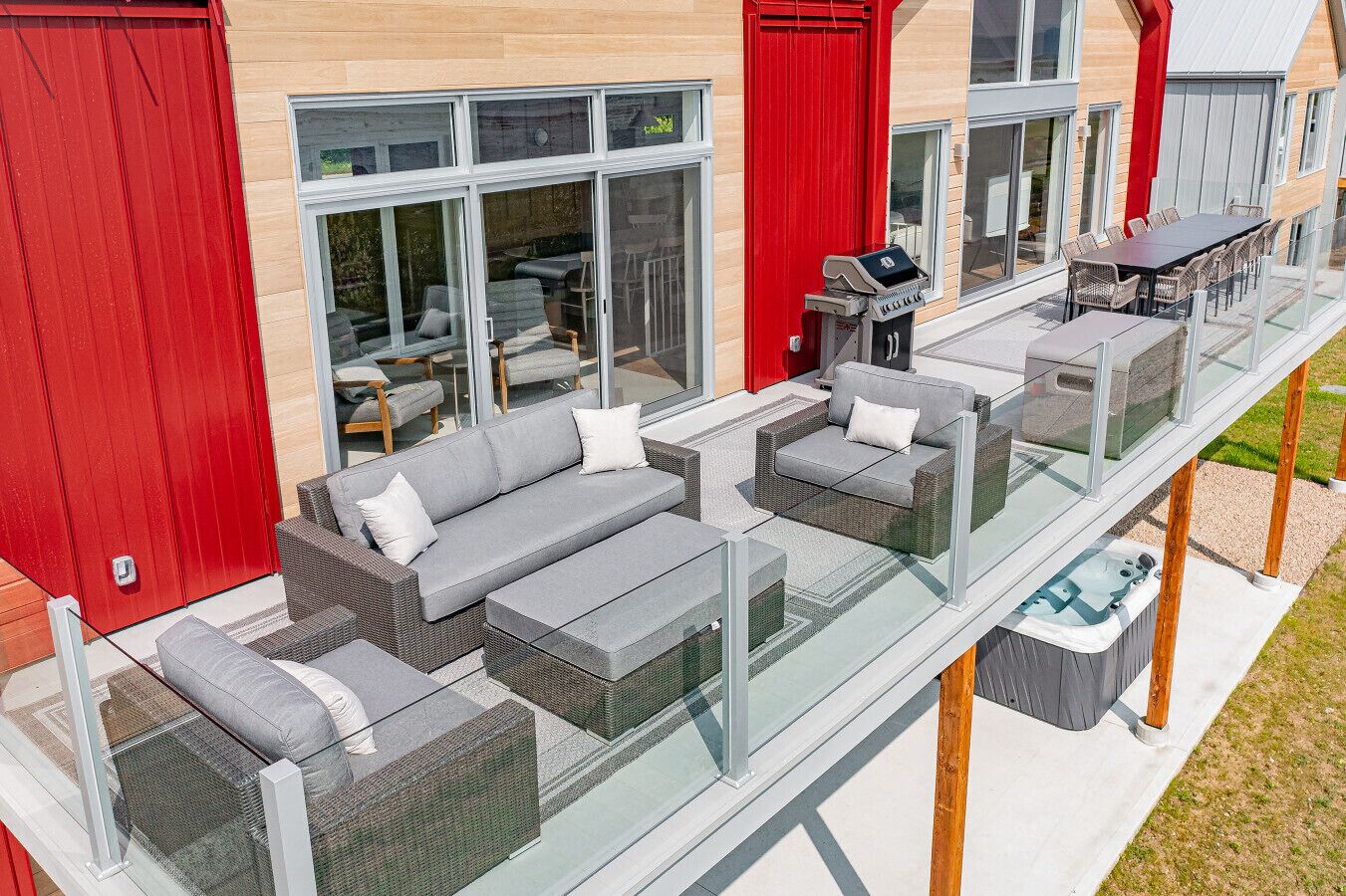 A modern outdoor living area with a glass balustrade, grey wicker furniture, and a hot tub.