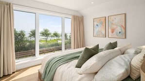 Ein Schlafzimmer mit großem Fenster, einem Bett mit vielen Kissen und zwei abstrakten Bildern an der Wand.