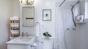 Un baño moderno con lavamanos, inodoro y ducha. Hay toallas y artículos de aseo en las repisas.