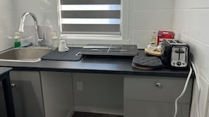 Eine Küche mit Spüle, einem Fenster mit Jalousien, einem Toaster und einer Nescafe-Kaffeemaschine.