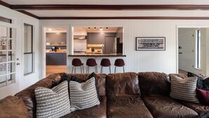 Ein modernes Wohnzimmer mit einem braunen Ledersofa, gemusterten Kissen und einer Küche im Hintergrund.