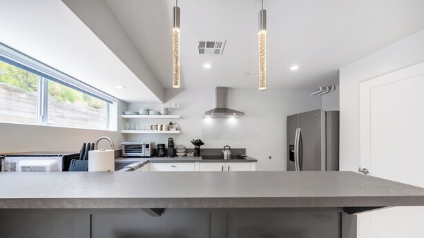 A modern kitchen with a central island, stainless steel appliances, pendant lighting, and a view of the outdoors.