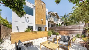 A modern outdoor patio with a wooden table, two cushioned chairs, and a sofa.