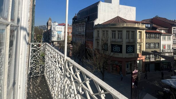 A balcony with ornate metal railings overlooking a street with historic buildings and a clear blue sky. - Casa Augusta 2 (Braga)