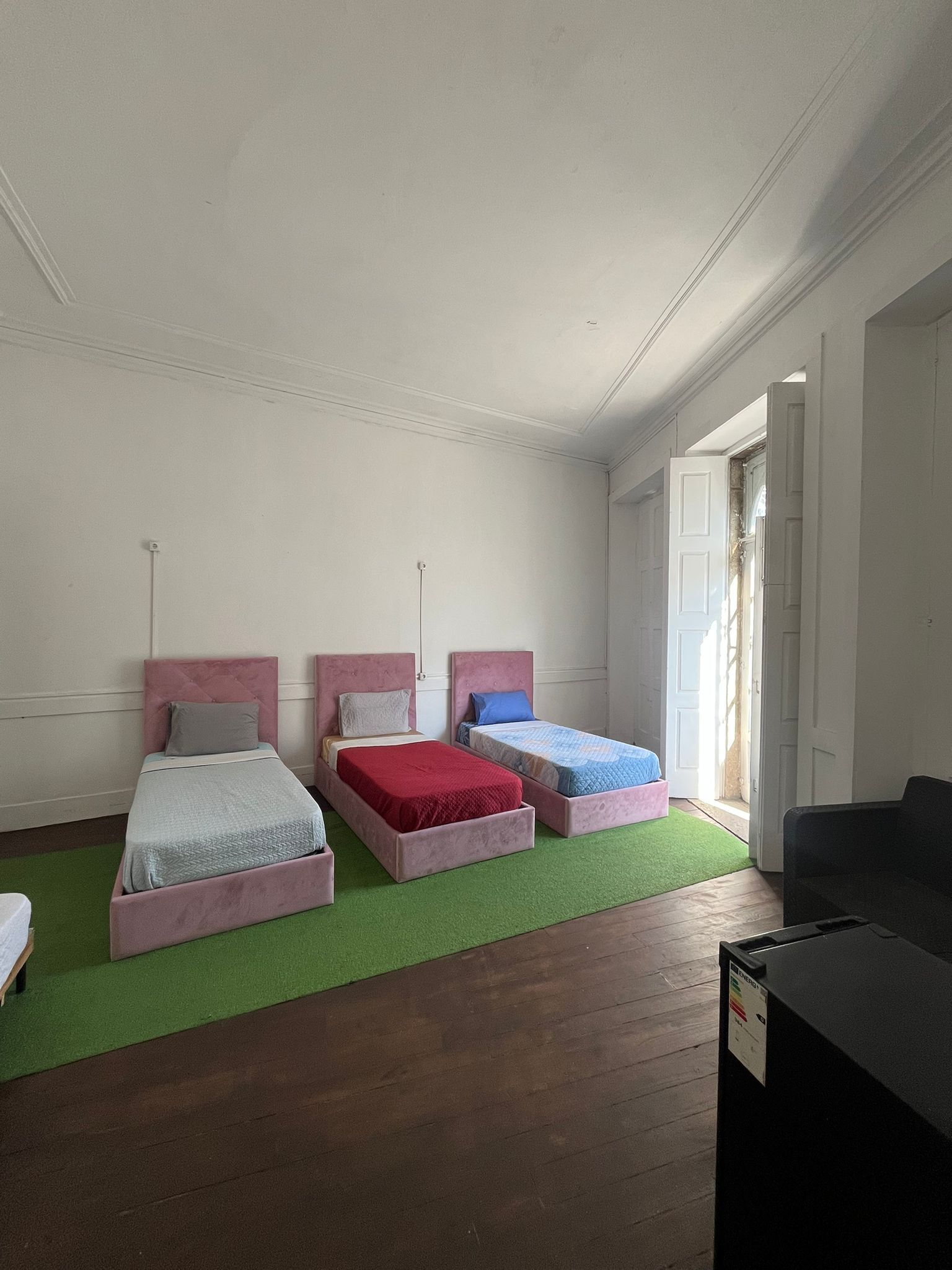 A room with three beds, a green carpet, wooden flooring, and a black piece of furniture.