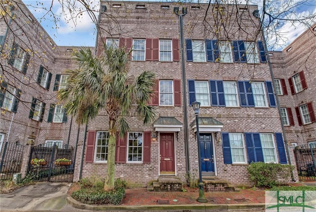 A multi-story brick building with red and blue shutters, a palm tree in the center, and a small garden area.