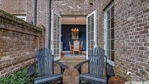 A narrow brick corridor with two wooden chairs facing a dining table and chairs. - Historic 3-Bed Townhouse w/ Courtyard & Parking (Savannah)