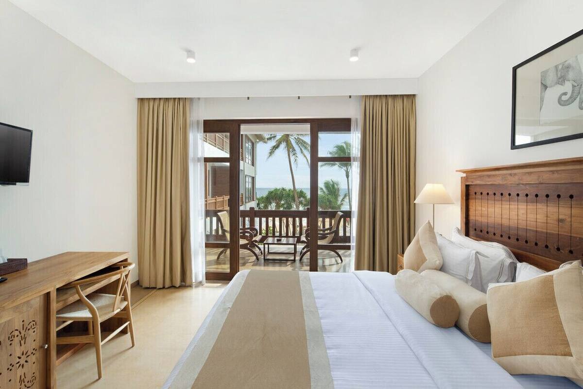 Ein Hotelzimmer mit Bett, Schreibtisch, Stuhl, Lampe und Meerblick durch große Fenster.