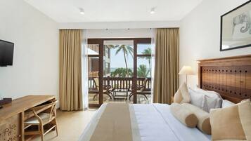 A hotel room with a bed, a desk, a chair, a lamp, and a view of the ocean through large windows.