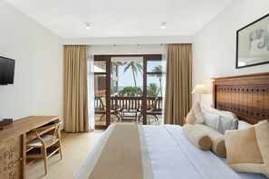 A hotel room with a bed, a desk, a chair, a lamp, and a view of the ocean through large windows. - The Lucky Elephant (Hikkaduwa)