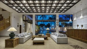 A spacious lobby with a pool view, striped sofas, a reception desk, and a wooden staircase. - The Lucky Elephant (Hikkaduwa)