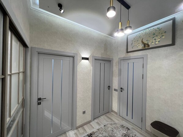 A hallway with three grey doors, a patterned rug, and a framed artwork on the wall. - Apartments Akay city 1 (Tashkent)