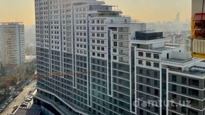 Een hoog gebouw met meerdere verdiepingen en balkons, omgeven door andere gebouwen en een heldere lucht.
