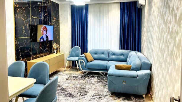 Een moderne woonkamer met een hoekbank, twee fauteuils, een salontafel en een televisie bevestigd aan een marmeren muur.