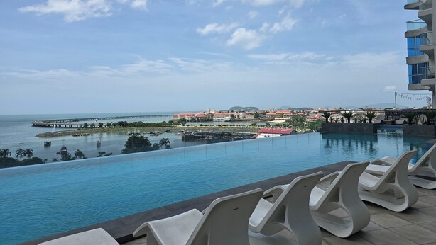A poolside view with lounge chairs, a clear sky, and a distant cityscape.