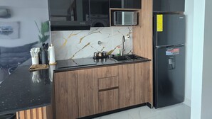 A modern kitchen with black cabinets, a microwave, a refrigerator, and a marble backsplash.