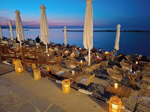 Buiten zitplaatsen met parasols en rieten stoelen, een stenen pad en uitzicht op zee.
