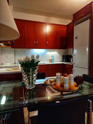 A kitchen with wooden cabinets, a refrigerator, a coffee maker, and a glass table with a candle arrangement.