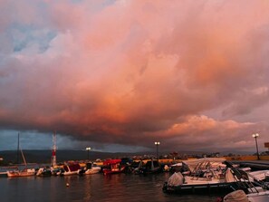 A marina with boats docked, a lighthouse, and a mountainous backdrop.