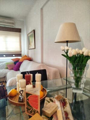 A hotel room with a bed, a bedside table with candles, a vase with flowers, and a lamp.