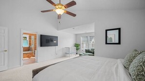 Un dormitorio con una cama grande, ventilador de techo, televisor y vistas al exterior.
