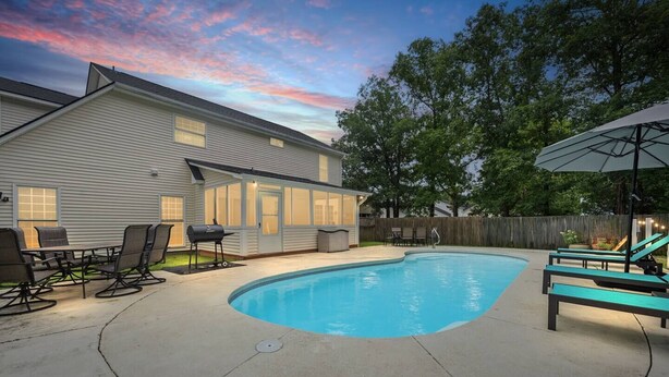 Un patio trasero con piscina, parrilla y mobiliario exterior.