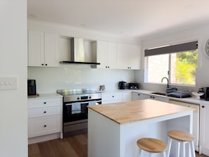 A modern kitchen with white cabinetry, a stainless steel stove, and a window with a view of greenery. - Tomaree Sands Family Townhouse in Nelson Bay (Nelson Bay)