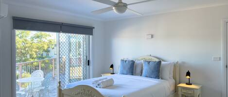Una camera da letto con un letto, una ventola a soffitto, un comodino con una lampada e un balcone con sedie.