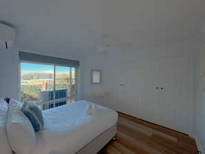 A bedroom with a large bed, a ceiling fan, a window with a view, and a white wardrobe.