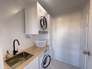 A compact laundry area with a washing machine, a dryer, a sink, and a basket.