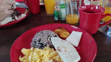 Un plato de desayuno con arroz, huevos revueltos, un wrap de tortilla y plátanos fritos.