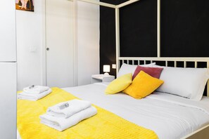 Ein ordentlich bezogenes Bett mit weißer und gelber Bettwäsche, ein weißer Kopfteil und ein kleiner Nachttisch mit Lampe.