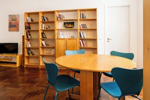 Una stanza con un tavolo in legno, quattro sedie, una libreria e un televisore.