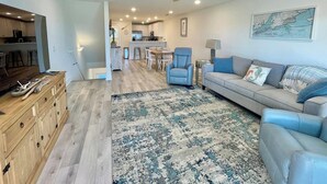 A spacious living area with a large sofa, a coffee table, and a dining area in the background. - ChilSea: Kayak, SUP, Views & more! (Pensacola)