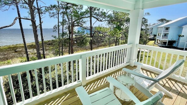 A wooden deck with white railings, two light blue chairs, and a view of the sea and trees. - ChilSea: Kayak, SUP, Views & more! (Pensacola)