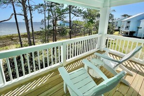 A wooden deck with white railings, two light blue chairs, and a view of the sea and trees. - ChilSea: Kayak, SUP, Views & more! (Pensacola)