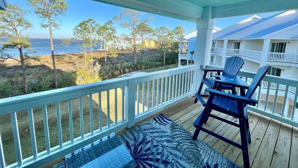 A covered outdoor area with a view of the beach, a wooden deck, and a blue chair. - Island Oasis: Beautiful Bay View, 2 Kayaks & Pool! (Pensacola)