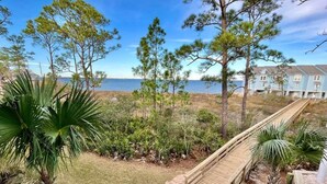 A wooden bridge leading to a beach area with a view of the ocean and a row of houses in the background. - Island Oasis: Beautiful Bay View, 2 Kayaks & Pool! (Pensacola)