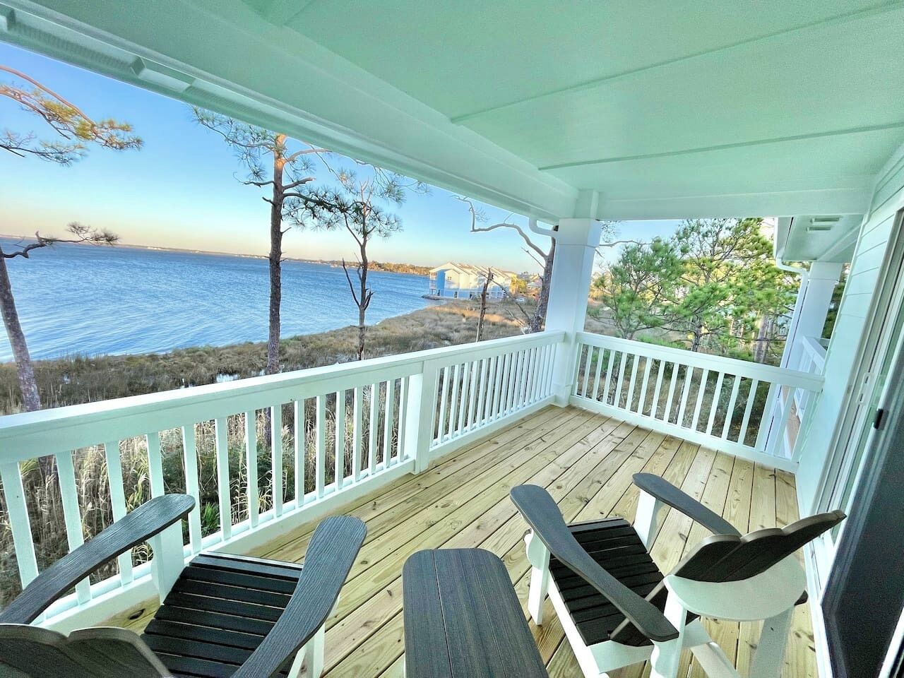 A covered porch with a view of the water, white railings, and two Adirondack chairs.